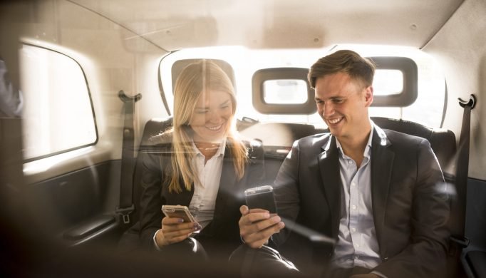 Businessman and businesswoman using smartphone in black cab, London, UK